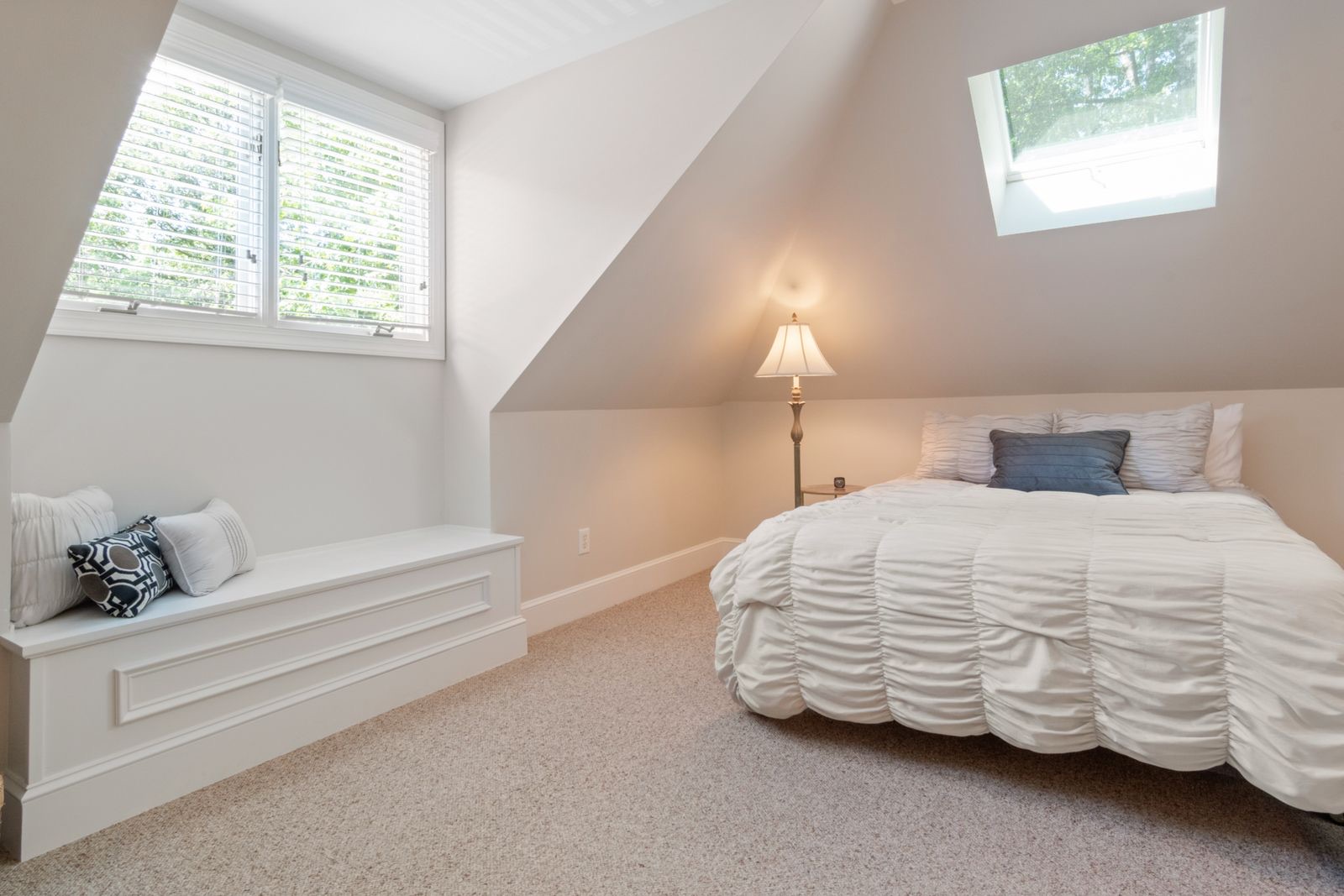 A bright white loft conversion bedroom with a sloped ceiling, rooflight and window seat